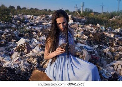 A Girl Among A Garbage Dump Looking Into An Empty Purse With Sadness