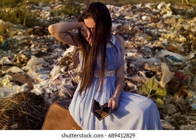 A Girl Among A Garbage Dump Wiping Her Tears While Holding An Empty Purse