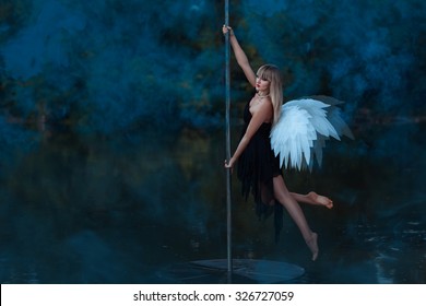 Girl with angel wings circling on a pole dance.  Around her smoke.