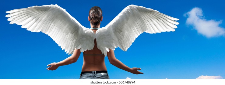 Girl with angel wings standing with spread arms against blue sky and white clouds. 