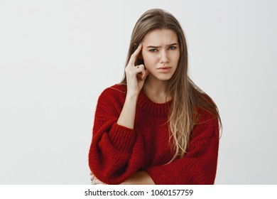 Girl Annoyed, Do Not Want Continue Conversation. Bothered Displeased Caucasian Female Entrepreneur In Loose Sweater, Holding Index Finger On Temple, Frowning, Doubtful And Confused Over Gray Wall