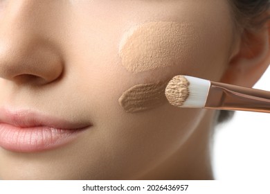 Girl applying foundation and concealer with brush on white background, closeup. Face contouring