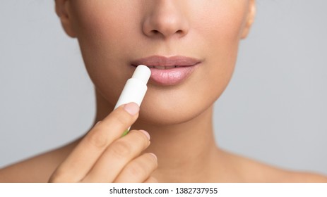 Girl applying hygienic lip balm on grey background, panorama