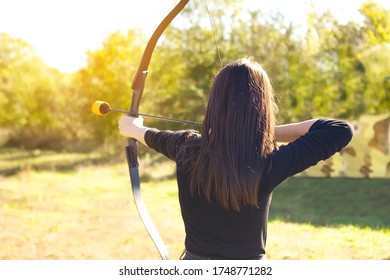 A girl Archer with a bow pulled the string shoots with her hands holding the arrow. the concept of sports archery, weapons and arrows. The view from the back