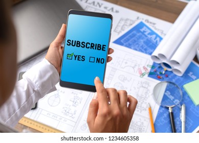 A girl (architect, student, businesswoman) at a table with business accessories, accessories for drawing (plans, rulers) and training with tablet with text Subscribe