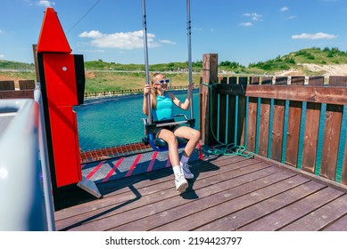 Girl Arrives On A Skydive Chair In A Mountain Adventure Park. Lake In Background