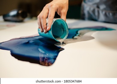 Girl artist pouring paint on paper making an art picture close up
