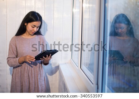 girl Asian appearance in a dress on a background of gray wall windows and reading a book