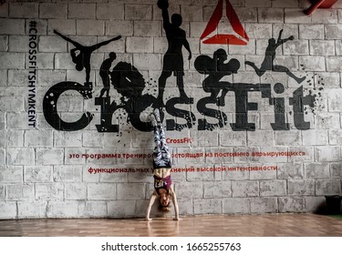 Girl Athlete Doing Crossfit In The Gym. A Woman Stands On Her Hands Against The Background Of The Wall With The Inscription CrossFit. Shymkent, Kazakhstan, May 22, 2018.