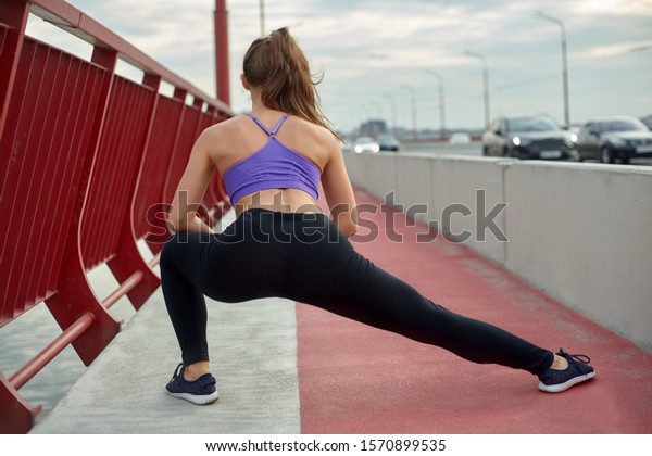 Girl athlete stretching in the\
morning outside, in the city, on modern bridge crossing river.\
Active healthy lifestyle. Sport and recreation\
concept.