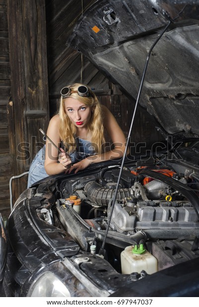 girl auto mechanic with a wrench near a broken\
car in the garage.