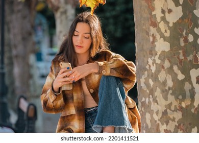 Girl In Autumn In The Park With Mobile Phone Or Smartphone