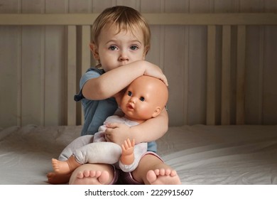 Girl and Baby Doll. Little Girl Playing on a White Blanket in Bedroom. Front View. Child Holding the Doll Toy. Family Relationship Concept. Kid Toddler is Alone, She Hugging and Cradling Her Toy. - Powered by Shutterstock