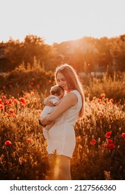 A girl with a baby. Mom and baby. The setting sun. Poppy flowers. Mom holds the baby in her arms. Summer day. A field of colors. Evening photo. A warm sunset.