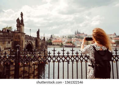 A girl with a backpack makes a photo on the phone of the Charles Bridge of Prague. Tourist girl takes pictures of Prague Castle. A woman holds a smartphone in her hands.