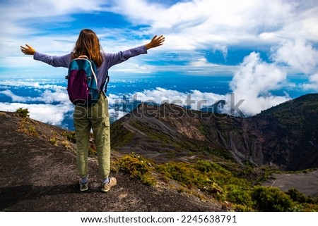 girl with backpack sits on top of volcano irazu in Costa Rica, volcanic landscape of Irazú Volcano National Park, massive volcano in clouds in Costa Rican mountains