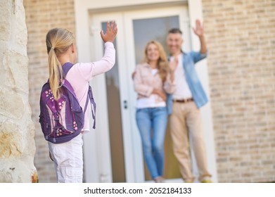 Girl With Backpack Waving Goodbye To Parents