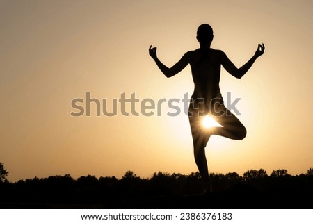 girl balancing on one leg doing yoga against the backdrop of the rising sun.