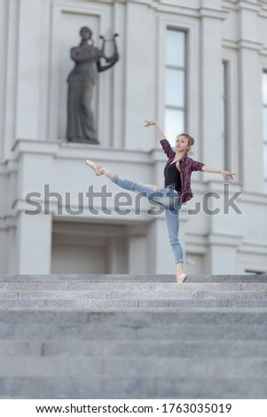 Girl ballerina in jeans, a plaid shirt and pointe shoes dancing in the city on the street