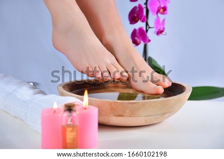 Girl bare feet on wooden bowl with water and decorative orchid flower and stone in beauty studio. Female foot with natural color. Pedicure and relaxation foot concept. Close up, selective focus