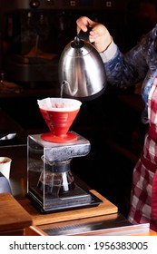 Girl barista brews coffee in red v60 pourover. Dripping water from funnel in hand into a server on electronic scale