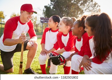 Girl baseball team kneeling in a huddle with their coach - Powered by Shutterstock