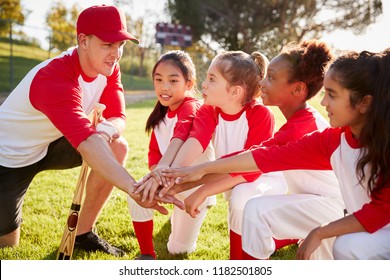 Girl baseball team kneeling with their coach, touching hands - Powered by Shutterstock