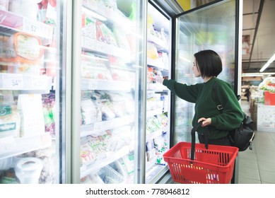 A girl with a basket takes frozen foods from the supermarket's refrigerator. The girl chooses goods in the store. Shopping in the supermarket. - Shutterstock ID 778046812
