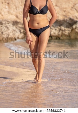 A girl in a bathing suit walks along the sandy beach near the sea.