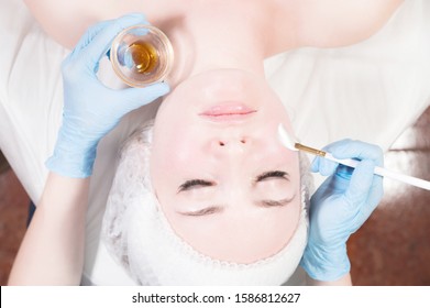 Girl beautician applies a brush to rejuvenate a mask on the face of an attractive girl in a spa salon. The concept of self-care and rejuvenation