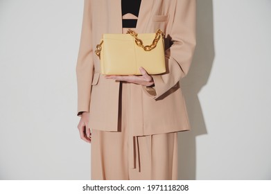 Girl in beautiful beige suit with luxury yellow leather handbag in her hands with massive gold chain. Horizontal fashion photo. Closeup. Shopping concept photo. Free space for logo or advert.