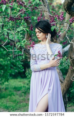 A girl in a beautiful elegant dress near a flowering lilac bush. Spring story at sunset. Botanical Garden.