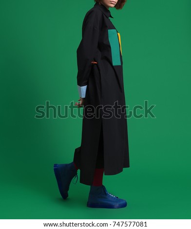 The girl in a beautiful, fashionable, luxurious black shirt, dress, robe, with yellow and green pockets, with different sleeves, and in blue shoes on a green background
