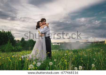 A girl in a beautiful gray dress hugs her beloved man in a field against a blue sky
