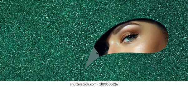 A Girl With Beautiful Green Eyes, With Bright Shadows On Her Eyelids. Looks Through A Teardrop Hole Made Of Green Shiny Paper.