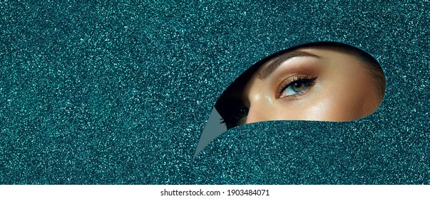 A Girl With Beautiful Green Eyes, With Bright Shadows On Her Eyelids. Looks Through A Teardrop Hole Made Of Green Shiny Paper.