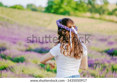 Girl with beautiful long hair and a lavender wreath on the lavender field. Nature blurred background