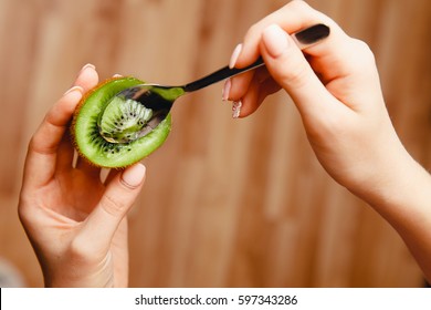 Girl With Beautiful Nails Is Eating Ripe Kiwi With Tea Dessert Spoon. Demonstration Of Fruit. Dark Background.