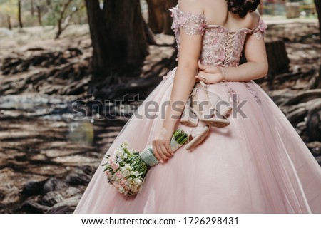 Girl in a beautiful pink dress, holding her flowers and shoes behind her.