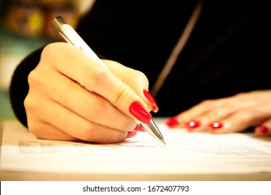 
A girl with beautiful red nails fills a document with a ballpoint pen. Female hand holds a ballpoint pen. - Shutterstock ID 1672407793