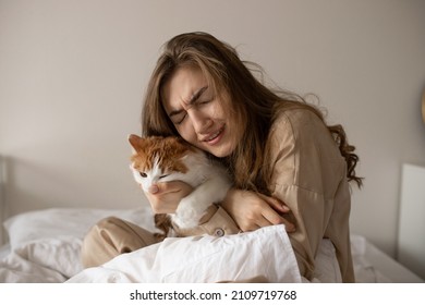 A girl in bed is bitten by a cat. A girl in pajamas sits in a bed with a cat. White-red cat.