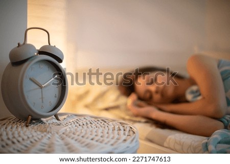 The girl in bed sleeps in the bedroom with an alarm clock on the cabinet next to her.