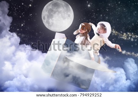A girl in the bedroom dressed as an airman or a pilot pretends to drive a paper airplane fly through the clouds and touch the stars and imagines she is flying free in the sky. 