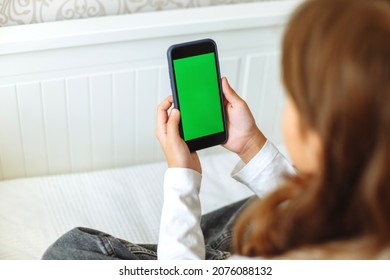 The girl behind the phone looks at the green screen.