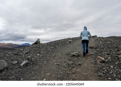 Girl From Behind Trekking On Black Lava Rocks In Iceland