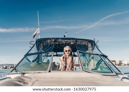 a girl behind the wheel of a boat stands and looks in the opening between the glasses