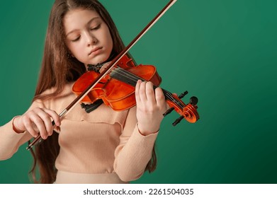 A girl in beige clothes plays the violin on a plain green background - Powered by Shutterstock