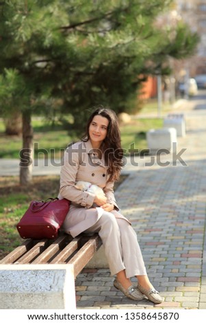 girl in a beige raincoat happy smiling on a bench with a dog little chihuahua