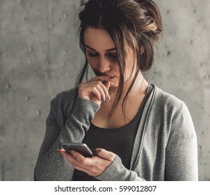 Girl being struck. Portrait of young girl with bruises on her face using a smart phone, on gray background