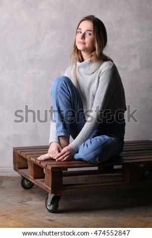 Girl with bended knee sitting on a deck. Gray background